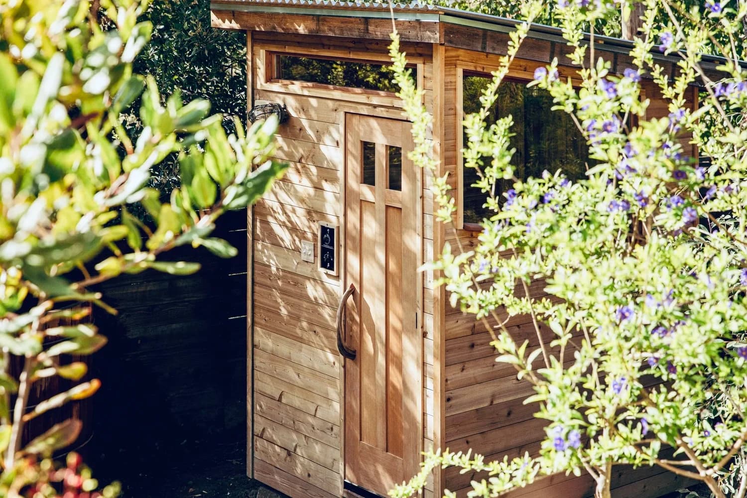 A handcrafted timber garden sauna surrounded by flowering plants.