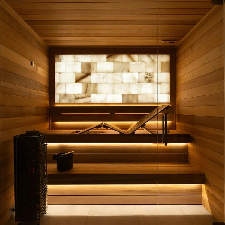 A compact timber sauna with warm lighting and a stone feature wall.